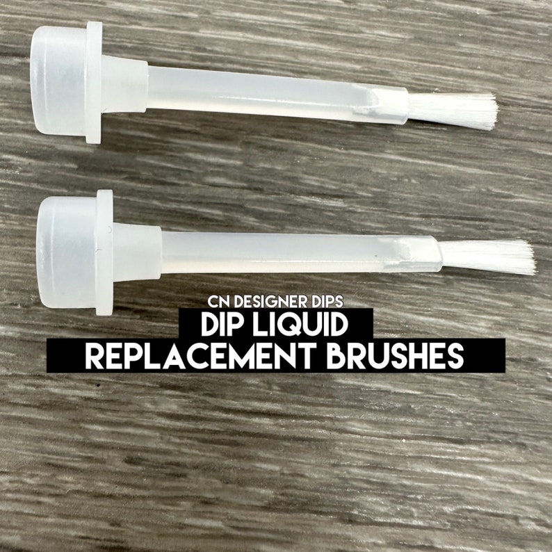 May include: Two clear plastic dip liquid replacement brushes. Each brush has a white bristle head and a long, thin stem. The text "CN DESIGNER DIPS DIP LIQUID REPLACEMENT BRUSHES" is printed in black on a black rectangle.