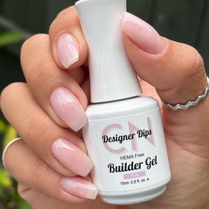 May include: A white bottle of pink builder gel nail polish with the text "Designer Dips HEMA Free Builder Gel Pink 15ml-0.5 fl. oz. e" on the label.