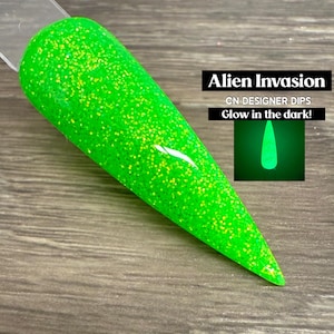 May include: A bright green nail dip with yellow glitter, labeled "Alien Invasion" and "Glow in the dark!" The nail dip is on a clear stick, with a glowing green nail tip graphic.