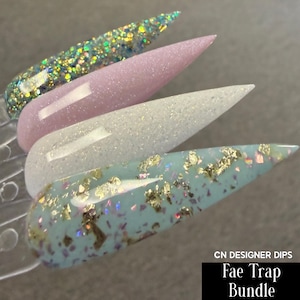 May include: Four acrylic nail tips in a row, each with a different design. The top tip is covered in iridescent glitter, the second is a light pink with shimmer, the third is white with glitter, and the bottom is light blue with gold flakes. The text "CN DESIGNER DIPS" and "Fae Trap Bundle" are in a black rectangle.