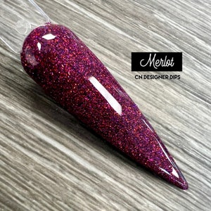 Könnte beinhalten: Nahaufnahme eines langen, spitzen, burgunderfarbenen Nagels mit glitzerndem Finish. Der Nagel ist mit "Merlot" und "CN Designer Dips" beschriftet.