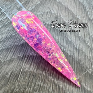 Op de afbeelding: Roze nageldippoeder met iriserende glitter en gouden vlokken. Het poeder is ge&euml;tiketteerd met "Love Blooms CN Designer Dips".