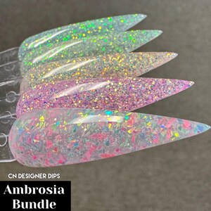 Puede incluir: Cinco muestras de polvo de inmersi&oacute;n para u&ntilde;as transparentes con purpurina iridiscente. Las muestras est&aacute;n dispuestas en fila, con la muestra m&aacute;s iridiscente en la parte inferior. El texto "CN DESIGNER DIPS Ambrosia Bundle" es visible en la parte inferior de la imagen.