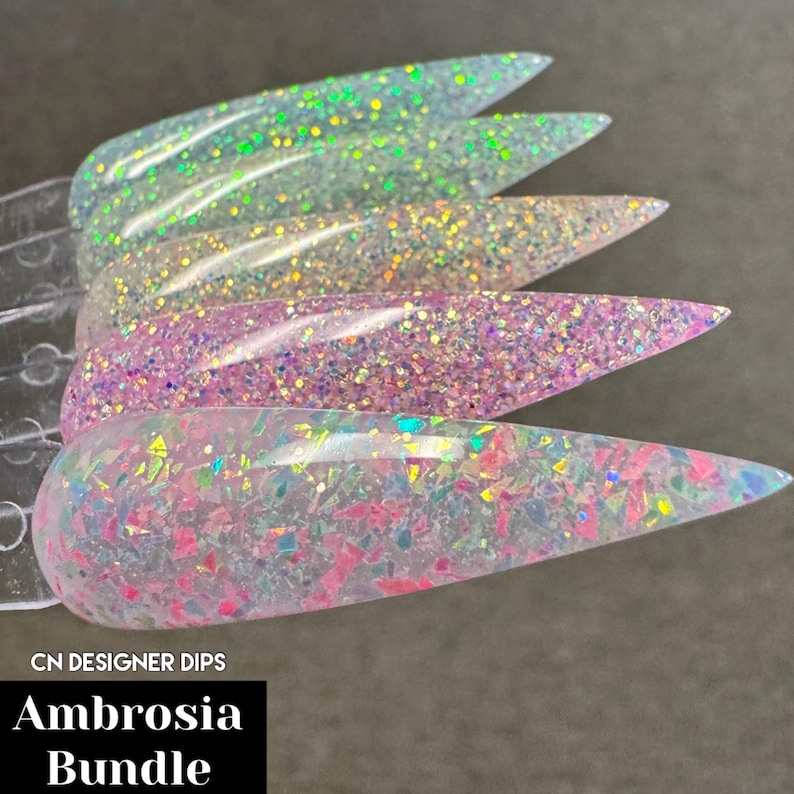Puede incluir: Cinco muestras de polvo de inmersi&oacute;n para u&ntilde;as transparentes con purpurina iridiscente. Las muestras est&aacute;n dispuestas en fila, con la muestra m&aacute;s iridiscente en la parte inferior. El texto "CN DESIGNER DIPS Ambrosia Bundle" es visible en la parte inferior de la imagen.
