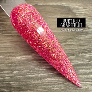 Puede incluir: Primer plano de un polvo de inmersión para uñas de color rosa con purpurina y acabado holográfico. El polvo está etiquetado como "Ruby Red Grapefruit" y "CN Designer Dips".