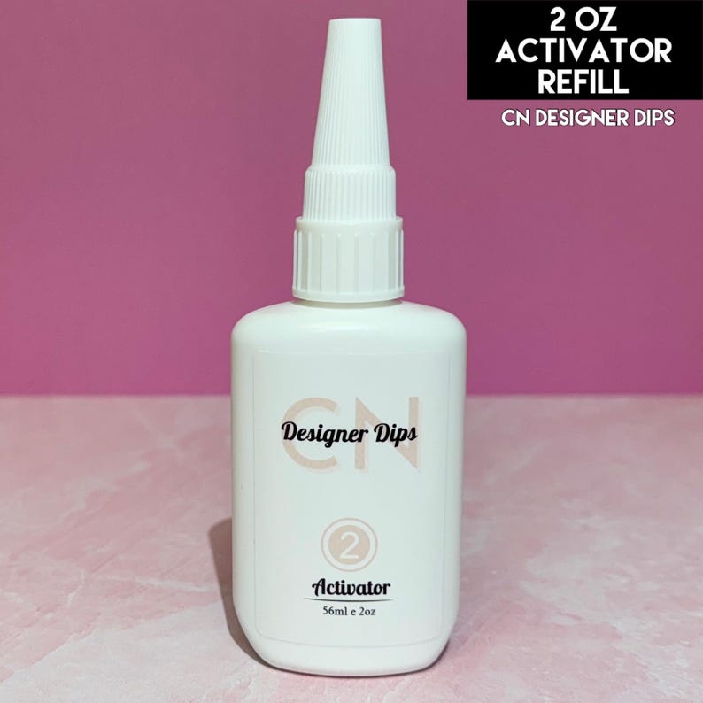 May include: A white plastic bottle with a white cap labeled "CN Designer Dips" and "Activator" with a number "2" on the label. The bottle contains 2 ounces of activator refill for dip powder nail polish.