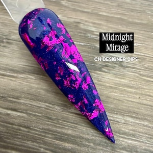 May include: A pointed nail swatch featuring a deep navy blue base with a shimmering finish, embedded with irregular bright magenta foil flakes. The text Midnight Mirage and CN DESIGNER DIPS is printed in white on the right side of the nail swatch.