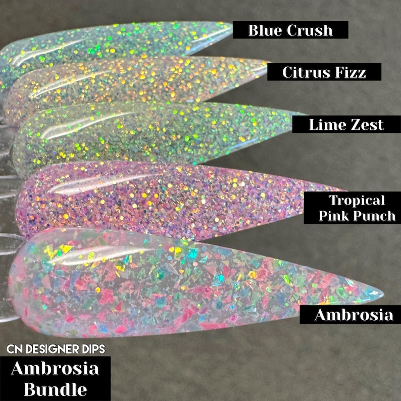 Puede incluir: Cinco botellas transparentes de polvo de inmersi&oacute;n para u&ntilde;as con purpurina iridiscente. Las botellas est&aacute;n etiquetadas con los nombres "Blue Crush", "Citrus Fizz", "Lime Zest", "Tropical Pink Punch" y "Ambrosia". El texto "CN DESIGNER DIPS Ambrosia Bundle" est&aacute; en la parte inferior de la imagen.