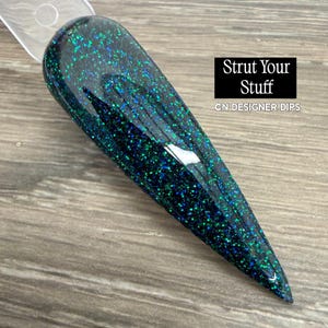 Puede incluir: Una muestra de uña larga y puntiaguda con una base oscura y purpurina verde y azul brillante. El texto "Strut Your Stuff" y "CN DESIGNER DIPS" se muestra sobre un fondo negro.
