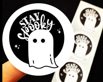 May include: A sheet of round stickers with a black and white design. The stickers feature a ghost with the text "Stay Spooky" in white lettering.