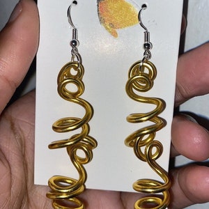 May include: A pair of gold-colored wire earrings with a spiral design. The earrings are hanging from silver hooks.