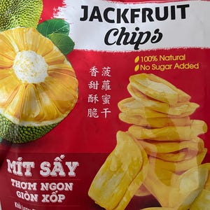 May include: A red bag of jackfruit chips with the words "JACKFRUIT Chips" in white. The bag features a sliced jackfruit and a pile of chips. Text on the bag includes "100% Natural" and "No Sugar Added". The net weight is 7 oz (200g).