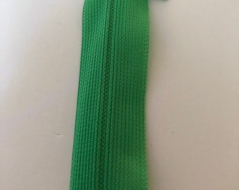 May include: A green zipper with a plastic slider. The zipper is closed and the slider is in the center of the zipper.