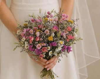 Könnte beinhalten: Ein farbenfroher Blumenstrauß mit rosa, lila, gelben und weißen Blüten. Der Strauß wird vor einem weißen Kleid gehalten. Die Blumen sind mit natürlichem Bindfaden zusammengebunden. Der Strauß ist eine Mischung aus verschiedenen Blumen und Grün.