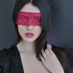 Könnte beinhalten: Eine Frau mit langen schwarzen Haaren, die einen schwarzen Satin-Morgenmantel und eine rote Spitzen-Augenmaske trägt.