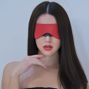 Könnte beinhalten: Eine Frau mit langen dunklen Haaren trägt eine rote Leder-Schlafmaske mit schwarzem Spitzenbesatz. Sie trägt ein schwarzes trägerloses Oberteil.