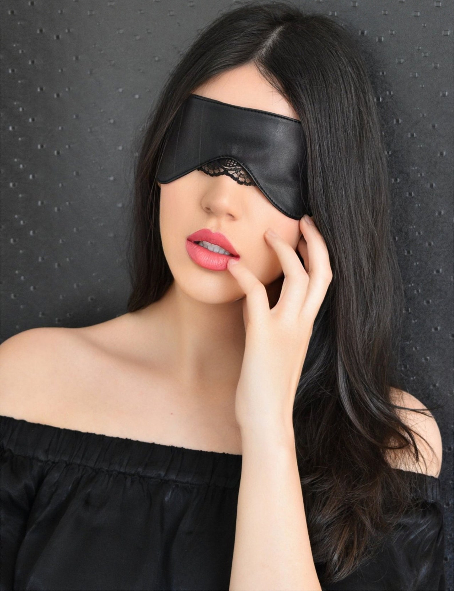 Close-up of woman wearing vegan leather eye mask with lace, posing with parted lips and dark hair.
