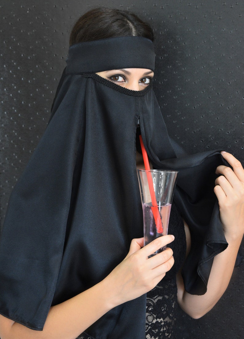 Peut inclure: Une femme portant un niqab noir tient un verre de liquide rose avec une paille rouge. Le verre est transparent et a une forme haute et mince.