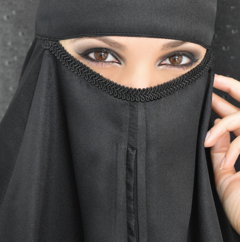 Peut inclure: Une femme portant un niqab noir avec une bordure d&eacute;corative. Ses yeux sont visibles &agrave; travers le tissu en maille.