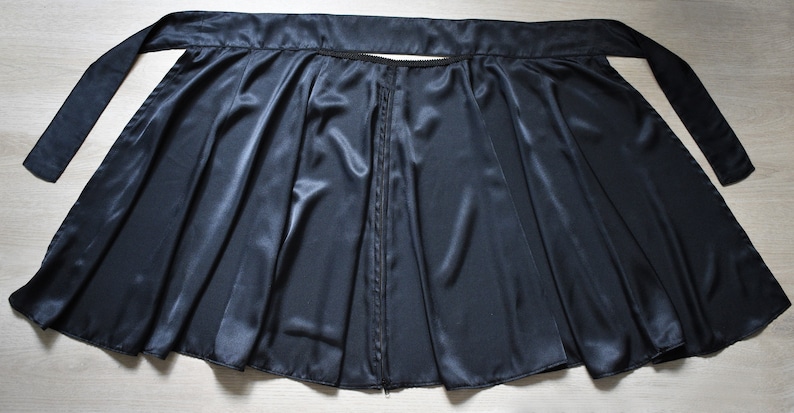 Peut inclure: Une jupe portefeuille en satin noir avec une fermeture &eacute;clair et une longue ceinture &agrave; nouer &agrave; la taille.