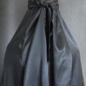 Peut inclure: Une cape en satin noir avec un design long et fluide. La cape est nou&eacute;e &agrave; l'arri&egrave;re du cou avec un n&oelig;ud.