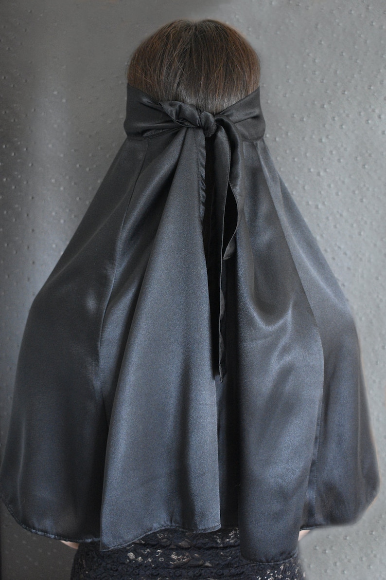 Peut inclure: Une cape en satin noir avec un design long et fluide. La cape est nou&eacute;e &agrave; l'arri&egrave;re du cou avec un n&oelig;ud.