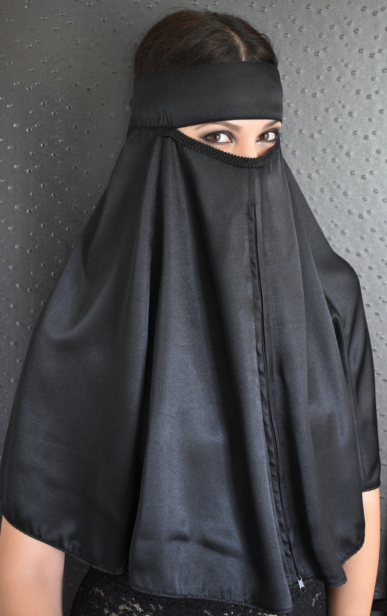 Peut inclure: Un niqab noir avec un design long et fluide. Le niqab est fait d'un tissu soyeux et a une petite ouverture pour les yeux.