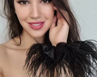 May include: A black feather boa with a satin ribbon tied around it. The boa is worn on a person's wrist.