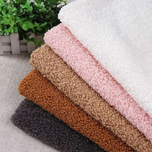 May include: A stack of five different coloured faux fur fabrics. The fabrics are white, pink, brown, tan, and grey.