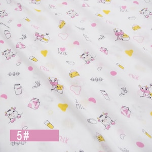 May include: White fabric with a repeating pattern of pink and yellow cows, milk bottles, hearts, and the words "I love milk".