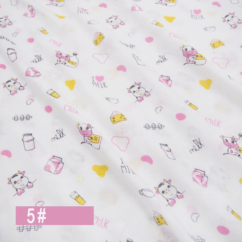 May include: White fabric with a repeating pattern of pink and yellow cows, milk bottles, hearts, and the words "I love milk".
