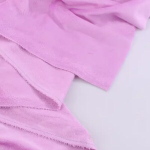 May include: Close-up of a soft, pale pink fabric with a slightly textured surface. The fabric is folded and has a raw edge.