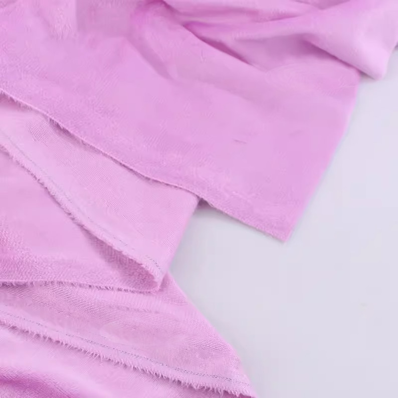 May include: Close-up of a soft, pale pink fabric with a slightly textured surface. The fabric is folded and has a raw edge.