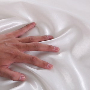 May include: A close-up of a smooth, white satin fabric. The fabric is soft and luxurious, with a subtle sheen.