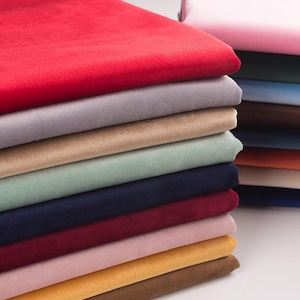 Puede incluir: Una pila de piezas de tela de terciopelo dobladas en varios colores, incluyendo rojo, gris, beige, verde claro, azul marino, burdeos, rosa claro y amarillo. La tela tiene una textura suave de pelo corto y está apilada verticalmente.