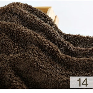 May include: Close-up of a brown, fluffy fabric with a soft, plush texture. The fabric is folded and draped over a wooden surface. The number "14" is visible in the lower right corner of the image.