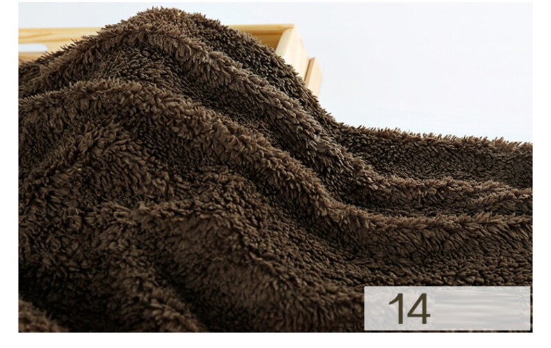 May include: Close-up of a brown, fluffy fabric with a soft, plush texture. The fabric is folded and draped over a wooden surface. The number "14" is visible in the lower right corner of the image.