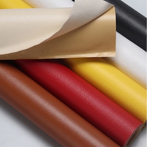 Peut inclure: Gros plan sur un assortiment de rouleaux de simili cuir de différentes couleurs, dont le marron, le rouge, le jaune, le blanc et le noir. Les rouleaux sont disposés en quinconce, le rouleau du haut étant partiellement déroulé pour révéler le matériau de support.