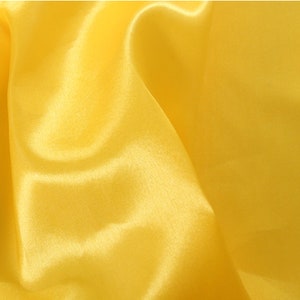 May include: A smooth, yellow satin fabric with a soft, luxurious texture. The fabric is draped and folded, creating a flowing and elegant look.