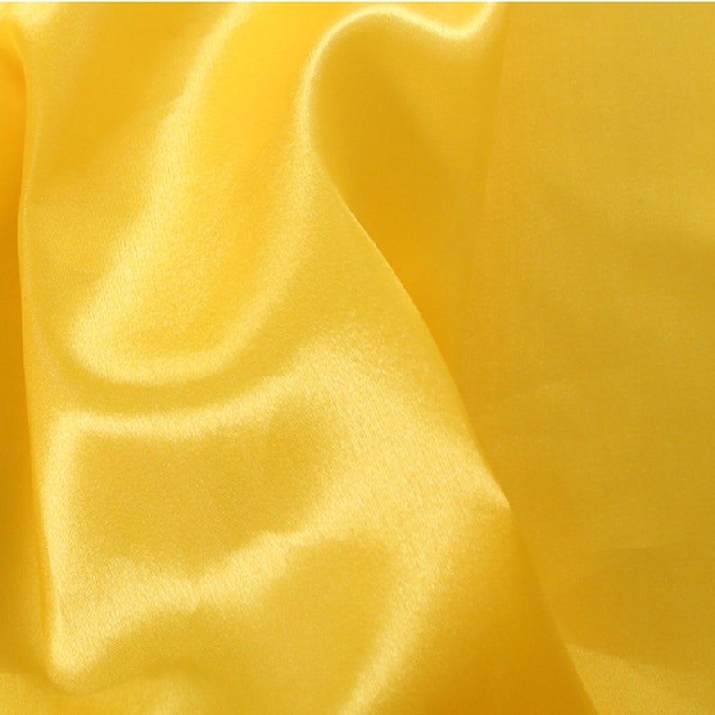 May include: A smooth, yellow satin fabric with a soft, luxurious texture. The fabric is draped and folded, creating a flowing and elegant look.