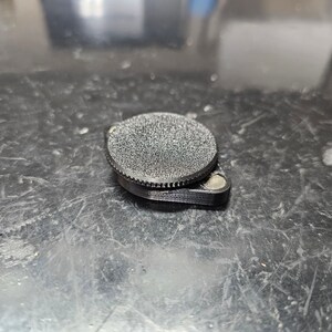 May include: A black, round, 3D printed object with a textured surface. The object has a smaller, flat, circular base.