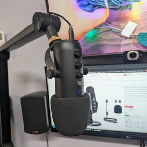 Puede incluir: Un micrófono negro con un filtro antipop y un brazo de suspensión. El micrófono tiene una luz azul en la parte delantera y varios botones para ajustar la configuración. El texto "ECHO", "MIC" y "LITE" es visible en el micrófono.