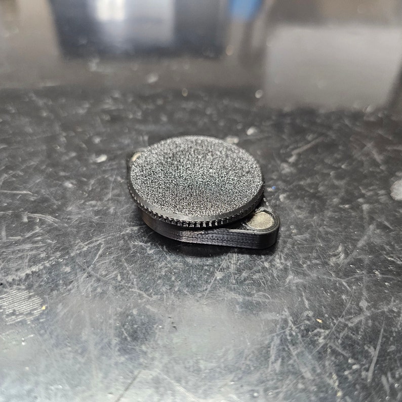 May include: A black, round, 3D printed object with a textured surface. The object has a smaller, flat, circular base.