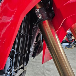 May include: Close-up of a red motorcycle with gold-coloured front forks and a black radiator grille.