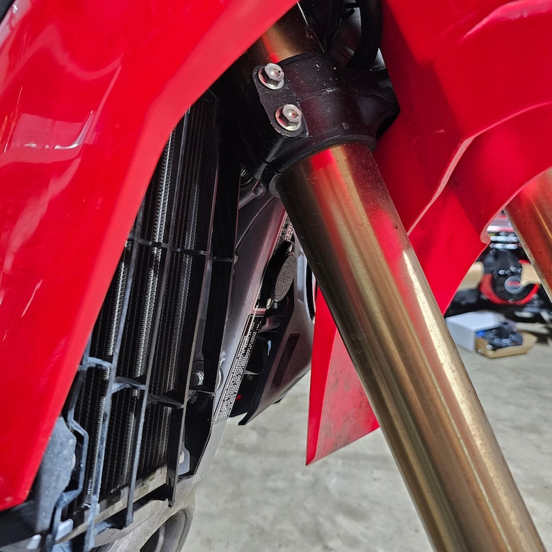 May include: Close-up of a red motorcycle with gold-coloured front forks and a black radiator grille.