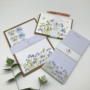 May include: A bluebell-themed stationery set with a notepad, writing paper, envelopes, and stickers. The set features a delicate floral design with bluebells, bees, and a mushroom.