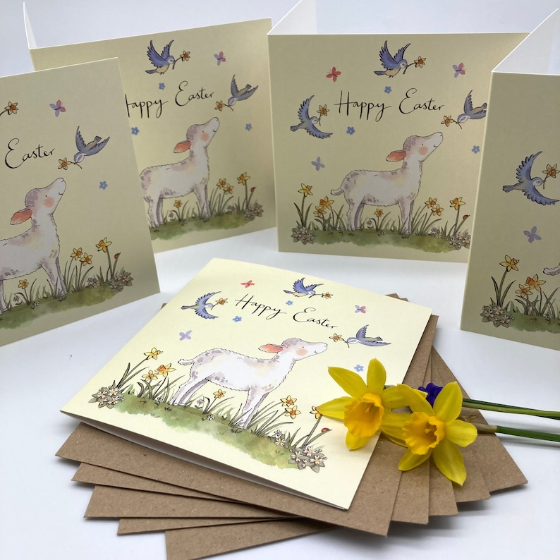 May include: A set of five Easter cards featuring a cute lamb in a field of daffodils with blue birds flying overhead. The cards are cream colored with a brown envelope.