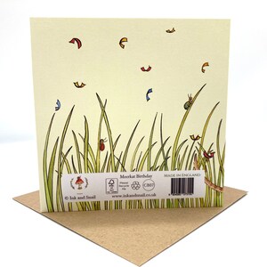 May include: A greeting card with a meerkat birthday theme. The card features a green and yellow illustration of tall grass with a red ladybug, a green beetle, and a few red and yellow leaves. The back of the card has a brown mushroom logo with the text "Ink and Snail" and the text "Meerkat Birthday" with a recycling symbol and the text "Made in England".