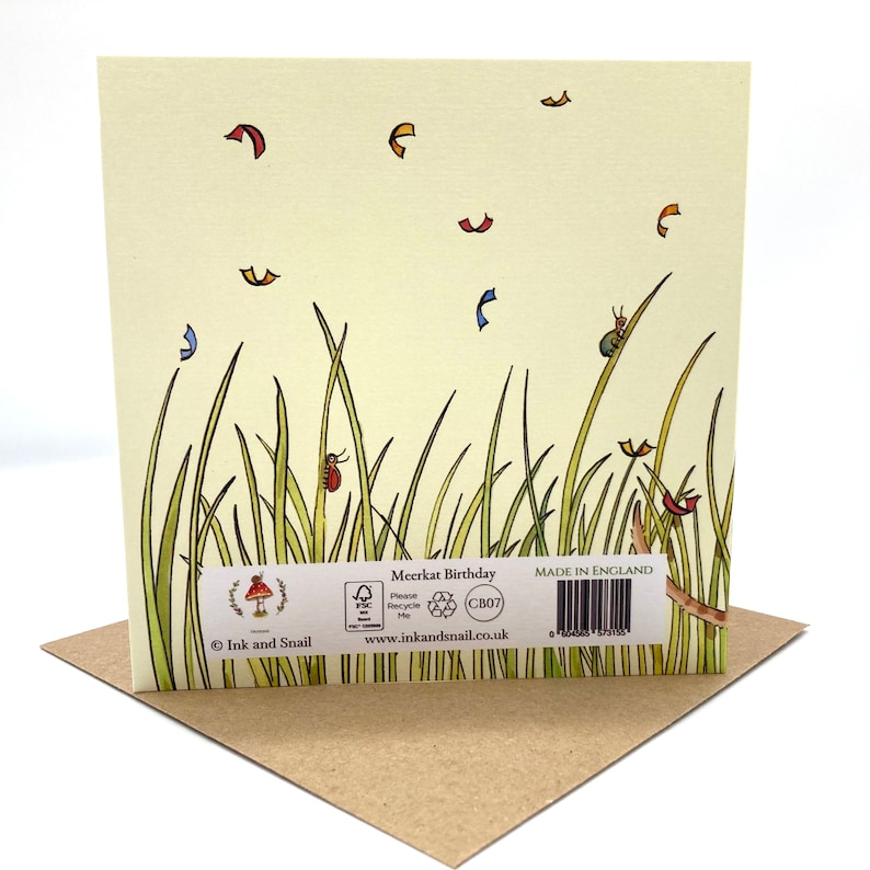 May include: A greeting card with a meerkat birthday theme. The card features a green and yellow illustration of tall grass with a red ladybug, a green beetle, and a few red and yellow leaves. The back of the card has a brown mushroom logo with the text "Ink and Snail" and the text "Meerkat Birthday" with a recycling symbol and the text "Made in England".