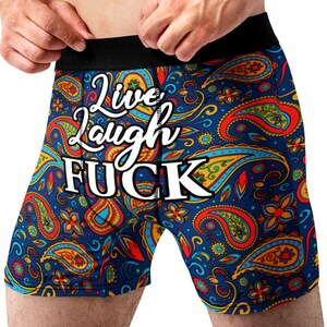 Könnte beinhalten: Blaue Boxershorts mit einem Paisley-Muster in Rot, Gelb und Türkis. Der Text "Live Laugh FUCK" ist weiß aufgedruckt. Der Bund ist schwarz.